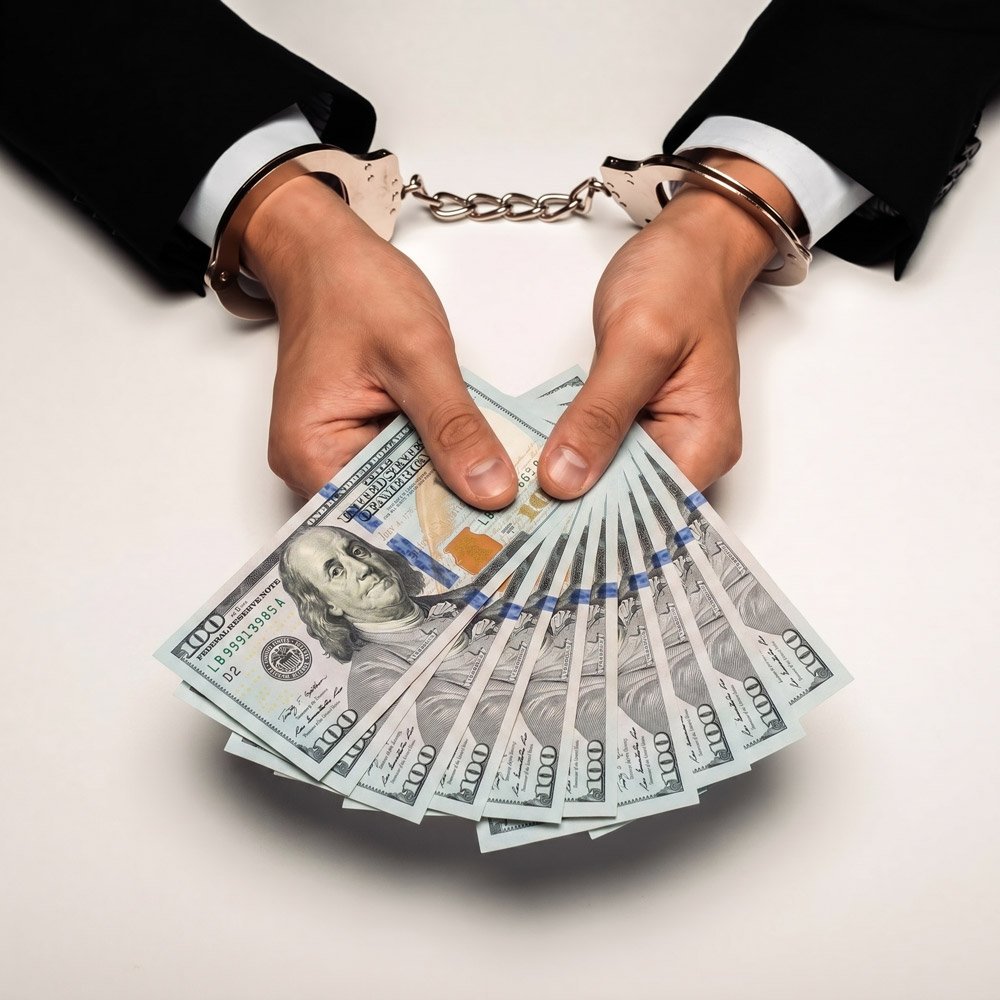 A handcuffed defendant holding a spread of hundred dollar bills in his hands symbolizing his need for a Bail Bondsman in Walhalla SC.
